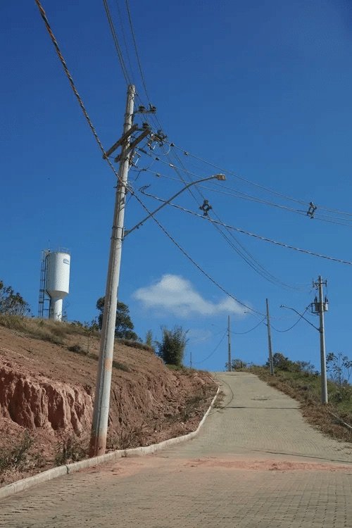 Poste com transformador e rede elétrica instalada ao longo da rua pavimentada do Portal de Bicas, em Bicas/MG