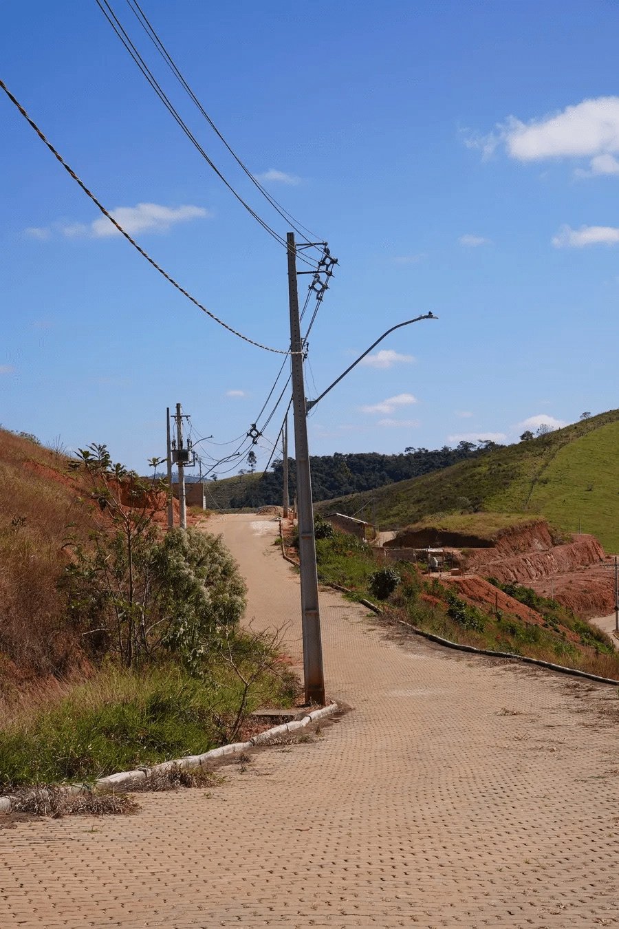 Rua pavimentada com bloco intertravado, meio-fio e postes de iluminação no Portal de Bicas, em Bicas/MG