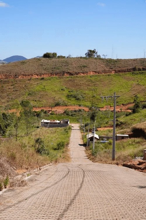Via pavimentada em declive no Portal de Bicas, com as primeiras construções ao fundo, em Bicas/MG